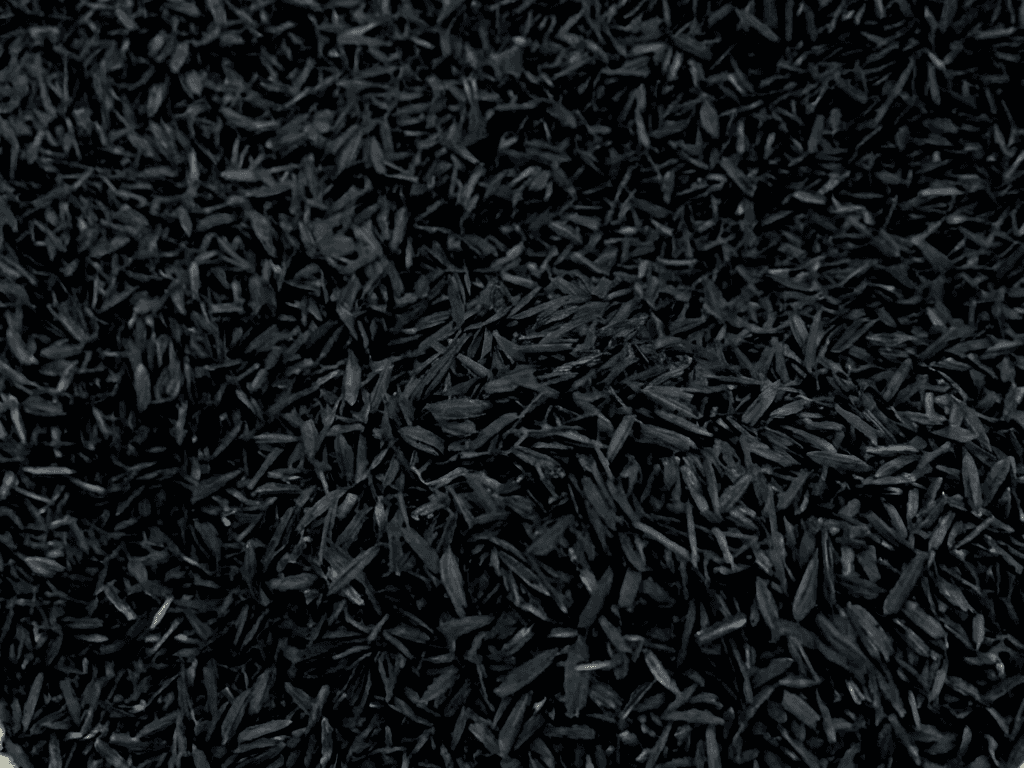Close-up of carbonized rice husk: a dense bed of dry black husks, each grain still holding its pointed shape.